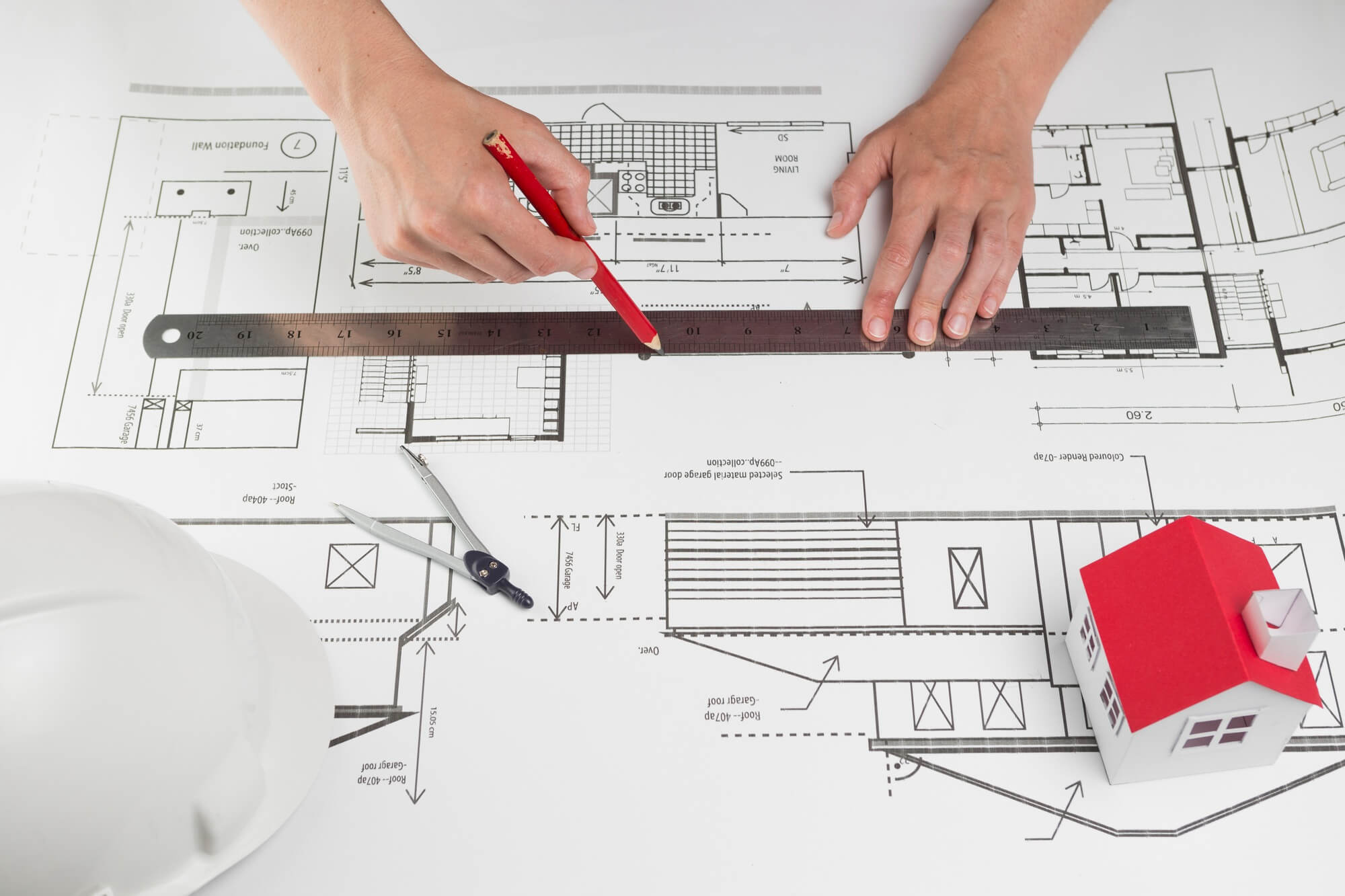 Architectural drawings, a hard hat, a ruler and a model house on a desk