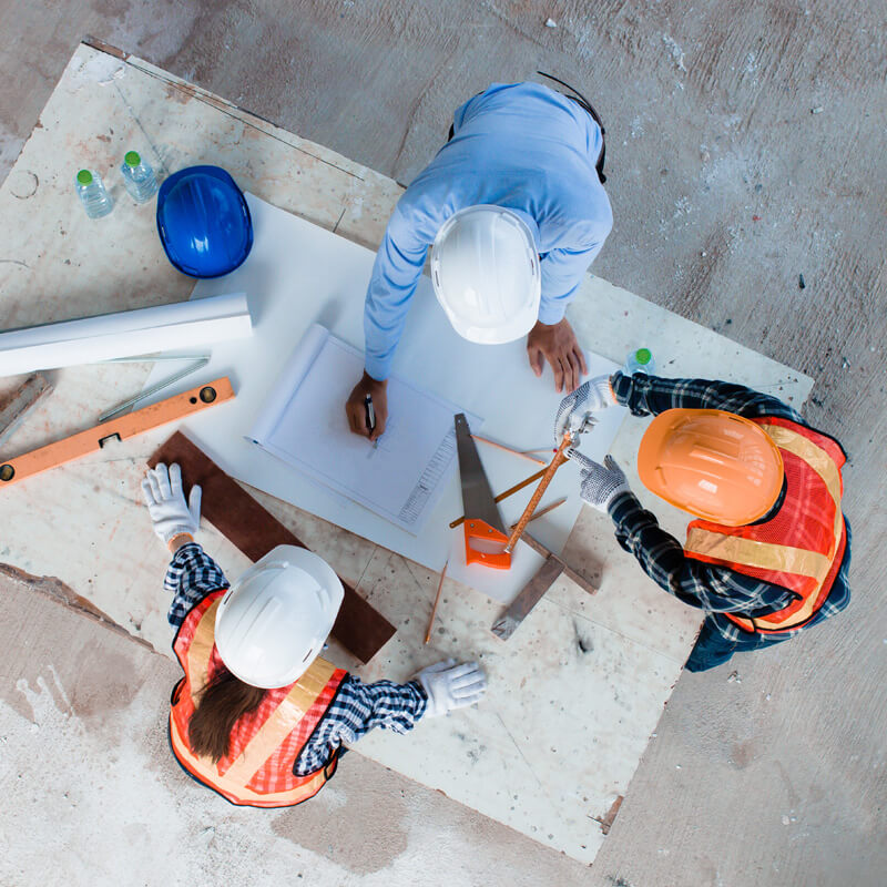 Three trades reviewing drawings on a site floor from above